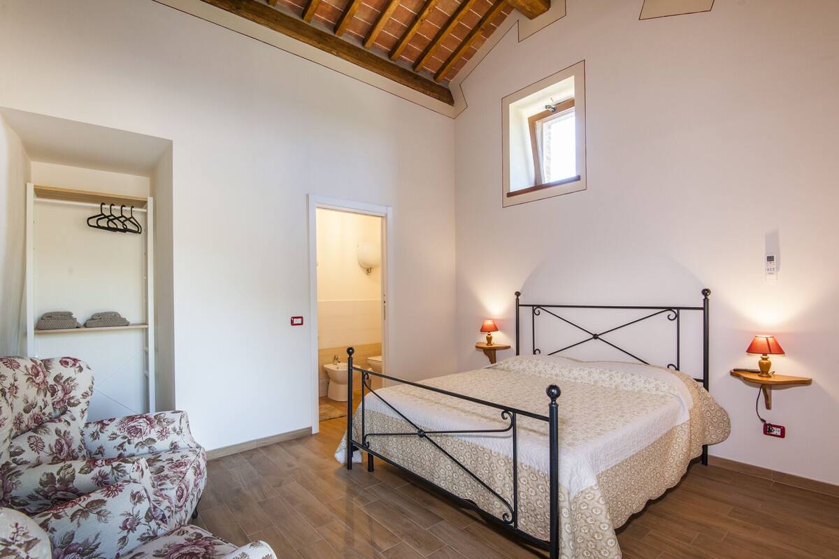 Une chambre à coucher avec un lit, des lampes de chevet, un plancher en bois, une armoire et une fenêtre.