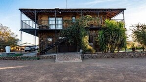 Un edificio rústico de piedra con un balcón de madera, una escalera y un camino de entrada pavimentado.
