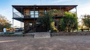 A rustic stone building with a wooden balcony, a staircase, and a paved driveway.