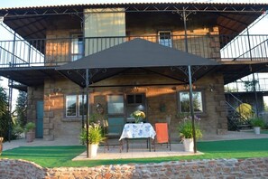 A stone building with a balcony, a covered patio with a table and chairs, and potted plants. - Kleynhans Home (Gaborone)