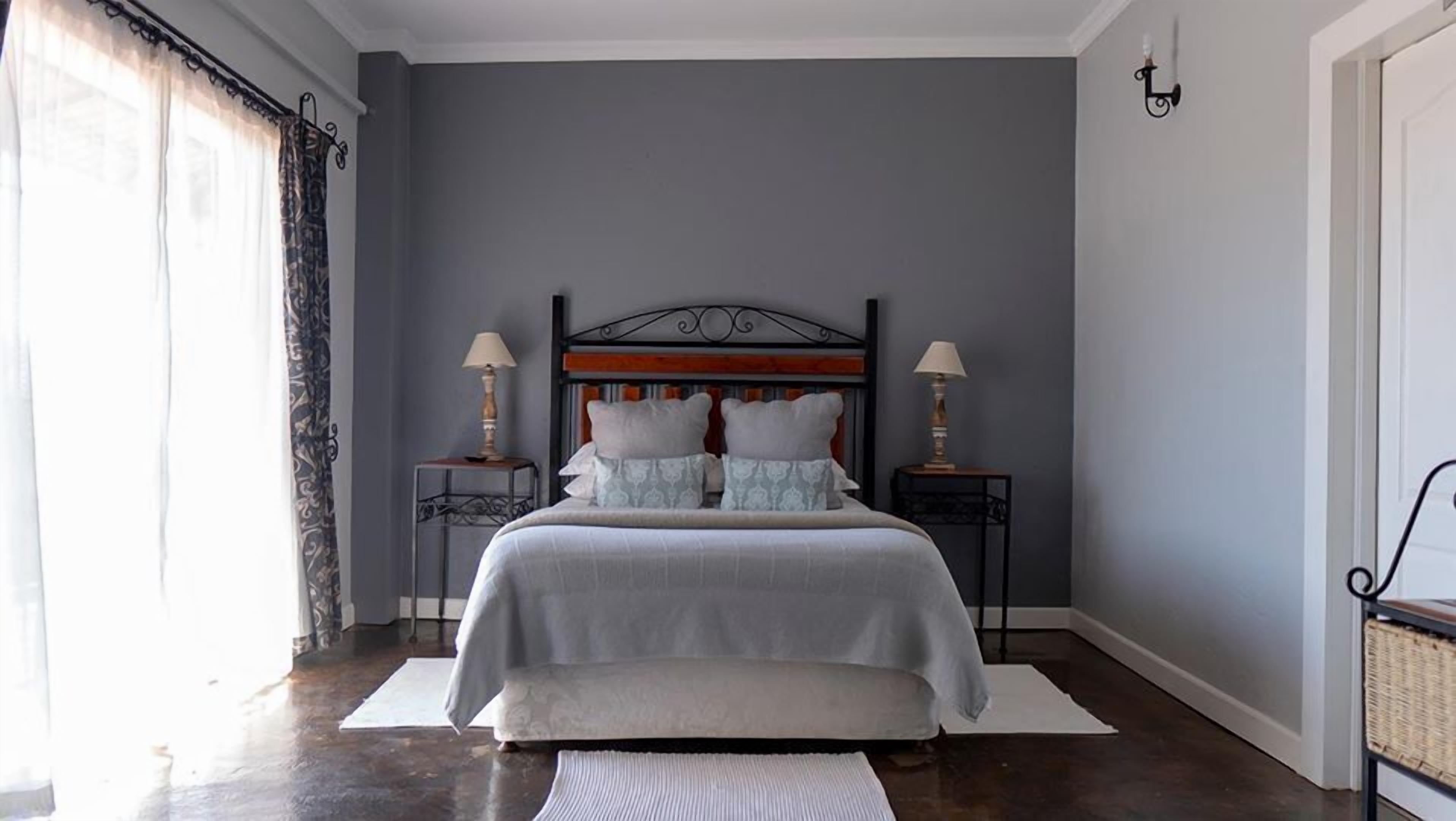 A bedroom with a large bed, two bedside tables with lamps, a headboard, and a window with curtains.