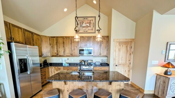A kitchen with wooden cabinets, a stainless steel refrigerator, a central island with stools, and pendant lighting. - Modern 3BR Mountain Retreat in North Keystone (Keystone)