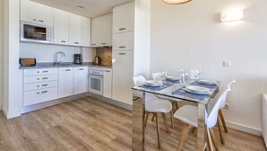 A modern kitchen with white cabinets, a built-in oven, and a dining area with a glass table and chairs. - APARTMENT IN CALA MILLOR, Modern, DIRECTLY ON THE BEACH, SEAVIEW, Wifi Incl, (Cala Millor)