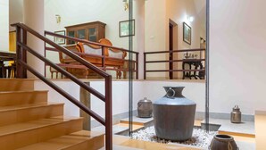 A staircase with wooden railings leading to a second floor. There is a large metal pot and two smaller metal containers on the floor. - Crystal Homestay by Vista Rooms (Virajpet)