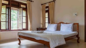 A neatly made bed with white linens in a room with a wooden bed frame, large windows with curtains, and a tiled floor. - Crystal Homestay by Vista Rooms (Virajpet)