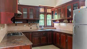 A kitchen with dark wooden cabinets, a stainless steel refrigerator, and a gas stove. - Crystal Homestay by Vista Rooms (Virajpet)