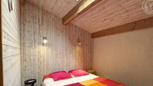 Une pièce aux murs en bois et au plafond incliné, un lit recouvert d’une couverture aux couleurs vives, une petite table ronde et un luminaire fixé au mur.