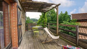 Une terrasse en bois avec une table et des chaises, un hamac et un fauteuil coloré.