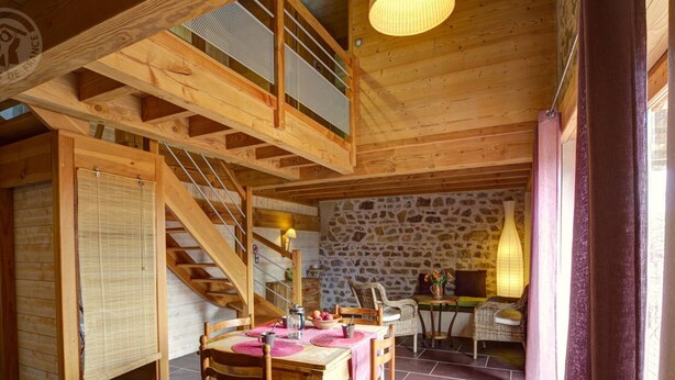 Un intérieur en bois avec un escalier, un mur en pierre et un coin repas comprenant des chaises et une table.