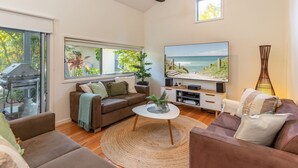 Ein Wohnzimmer mit großem Fernseher, einer Couch, einem Couchtisch und einem Grill vor dem Fenster.