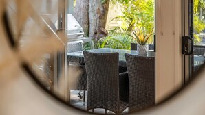 Ein Essbereich im Freien mit Korbmöbeln und einem Grill, mit Blick auf einen Garten mit verschiedenen Pflanzen.
