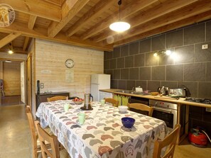 Une cuisine et un coin repas chaleureux, avec des poutres en bois, un dosseret carrelé et une table mise avec de la vaisselle et une bouilloire.