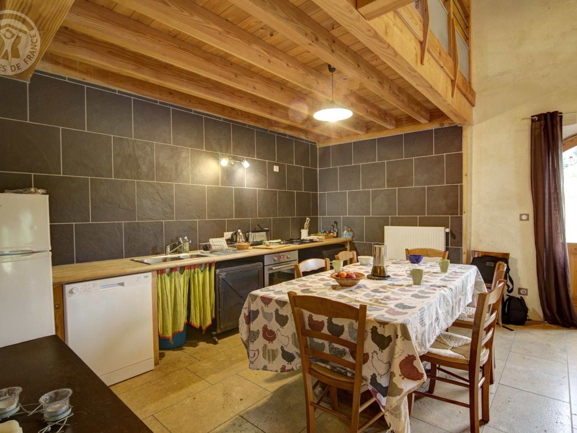 A kitchen with a wooden ceiling, a tiled backsplash, a sink, a stove, and a dining table with chairs.