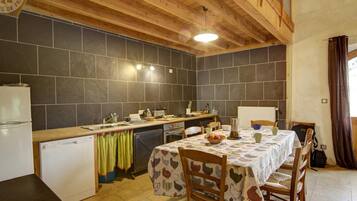 A kitchen with a wooden ceiling, a tiled backsplash, a sink, a stove, and a dining table with chairs.