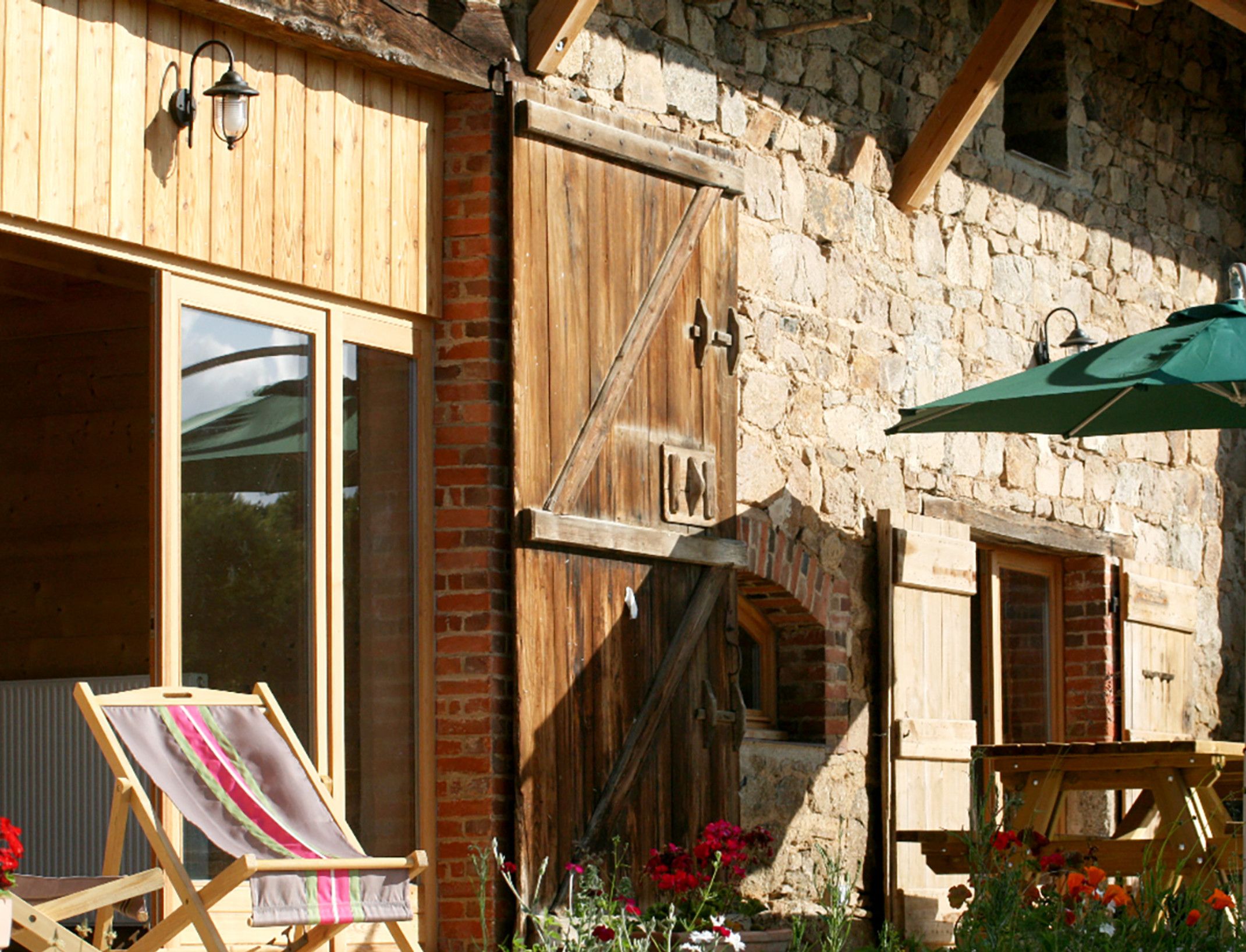 A rustic building with wooden shutters, a stone wall, and a green umbrella.