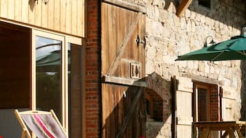 A rustic building with wooden shutters, a stone wall, and a green umbrella.