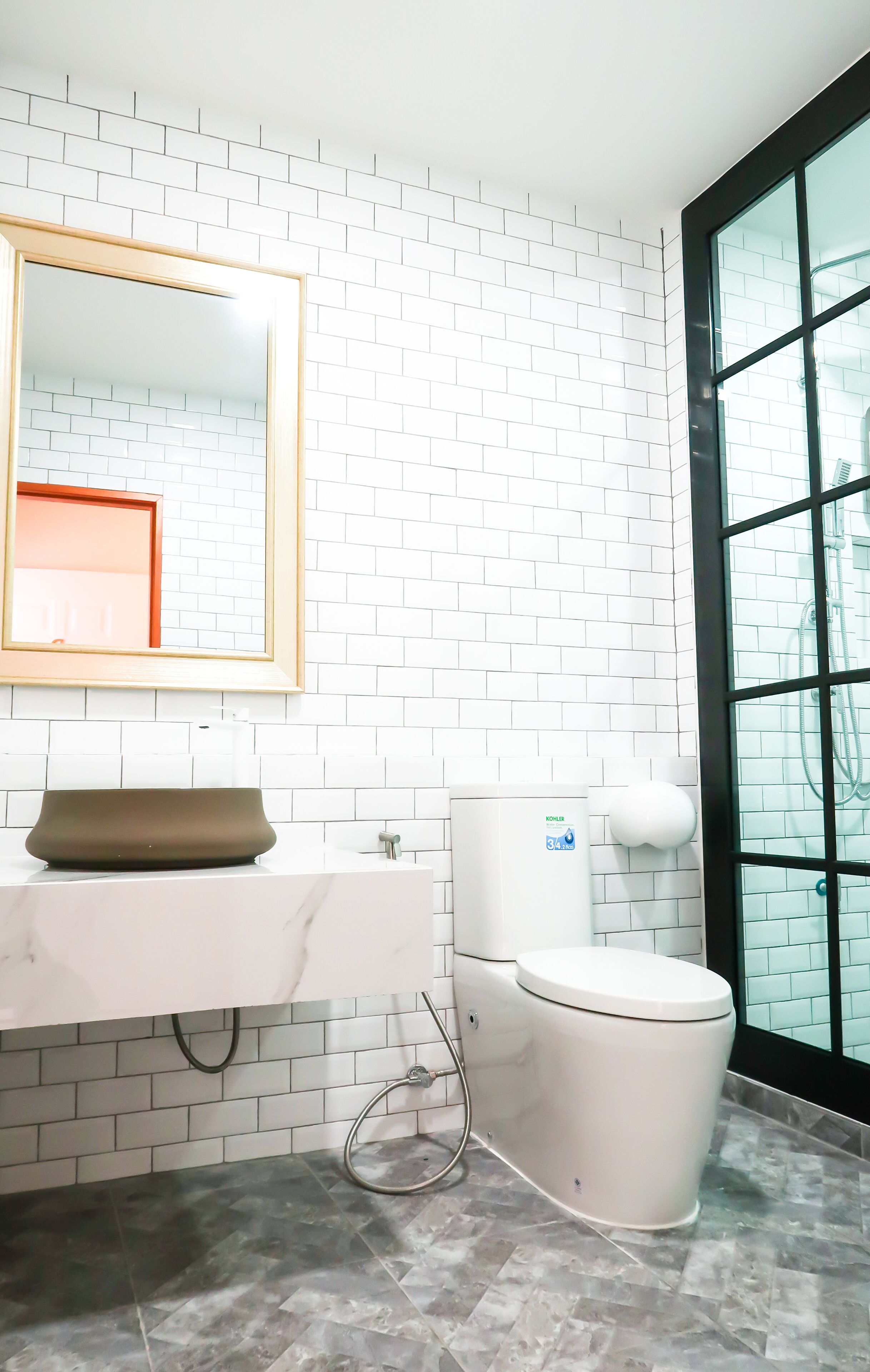 A modern bathroom with white subway tiles, a marble countertop, a toilet, and a large window.