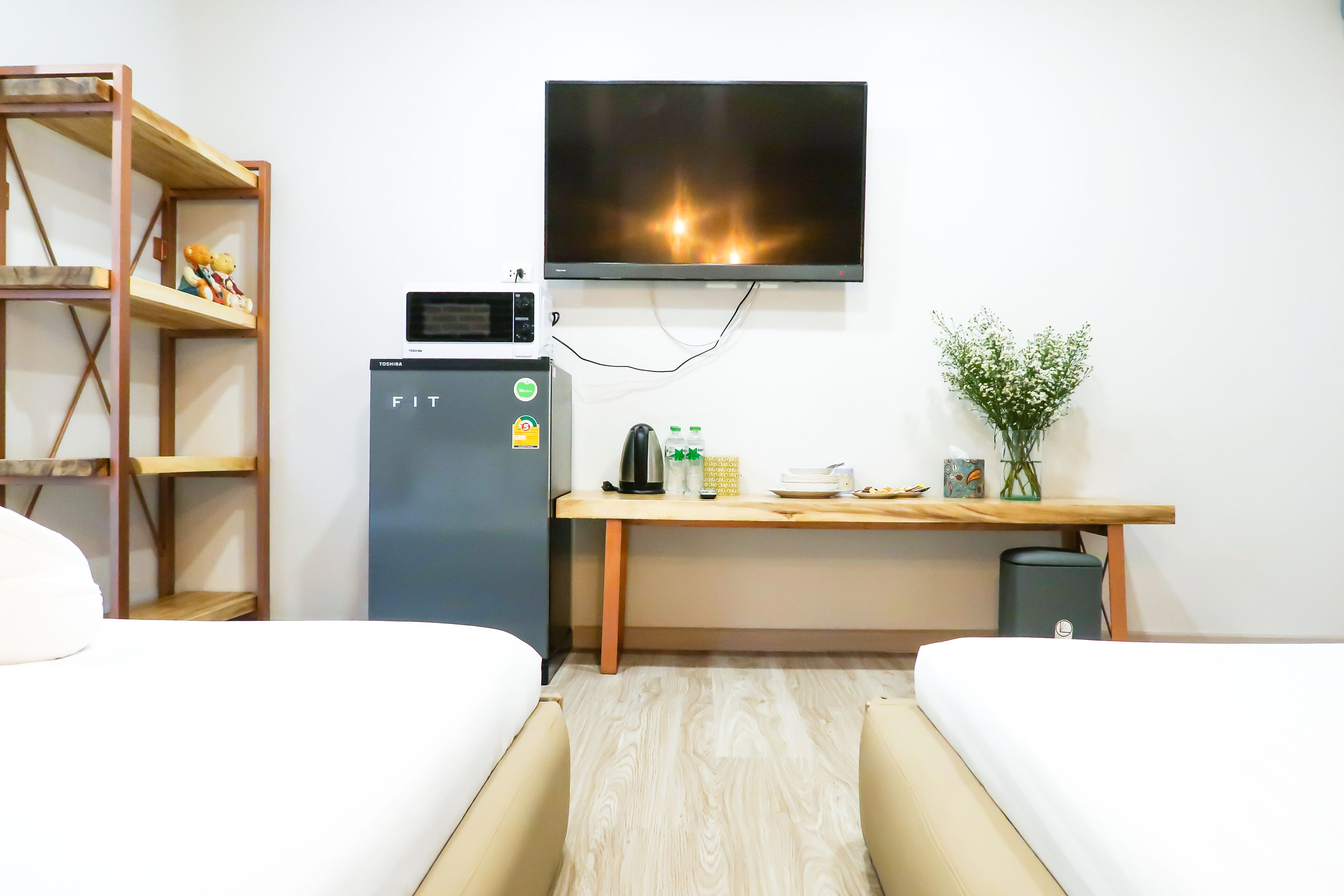 A hotel room with a bed, a desk with a TV, a mini-fridge, and a shelf with decorative items.