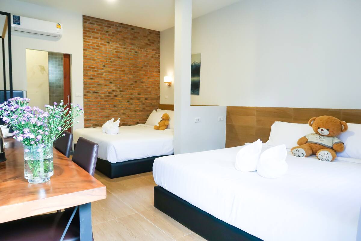 Een hotelkamer met twee bedden, een houten tafel met een bloevas en een teddybeer op een van de bedden.