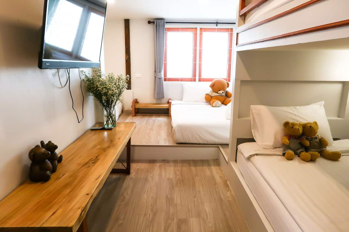 Een hotelkamer met een houten bureau, een aan de muur bevestigde televisie, een bed met twee teddyberen en een raam met gordijnen.