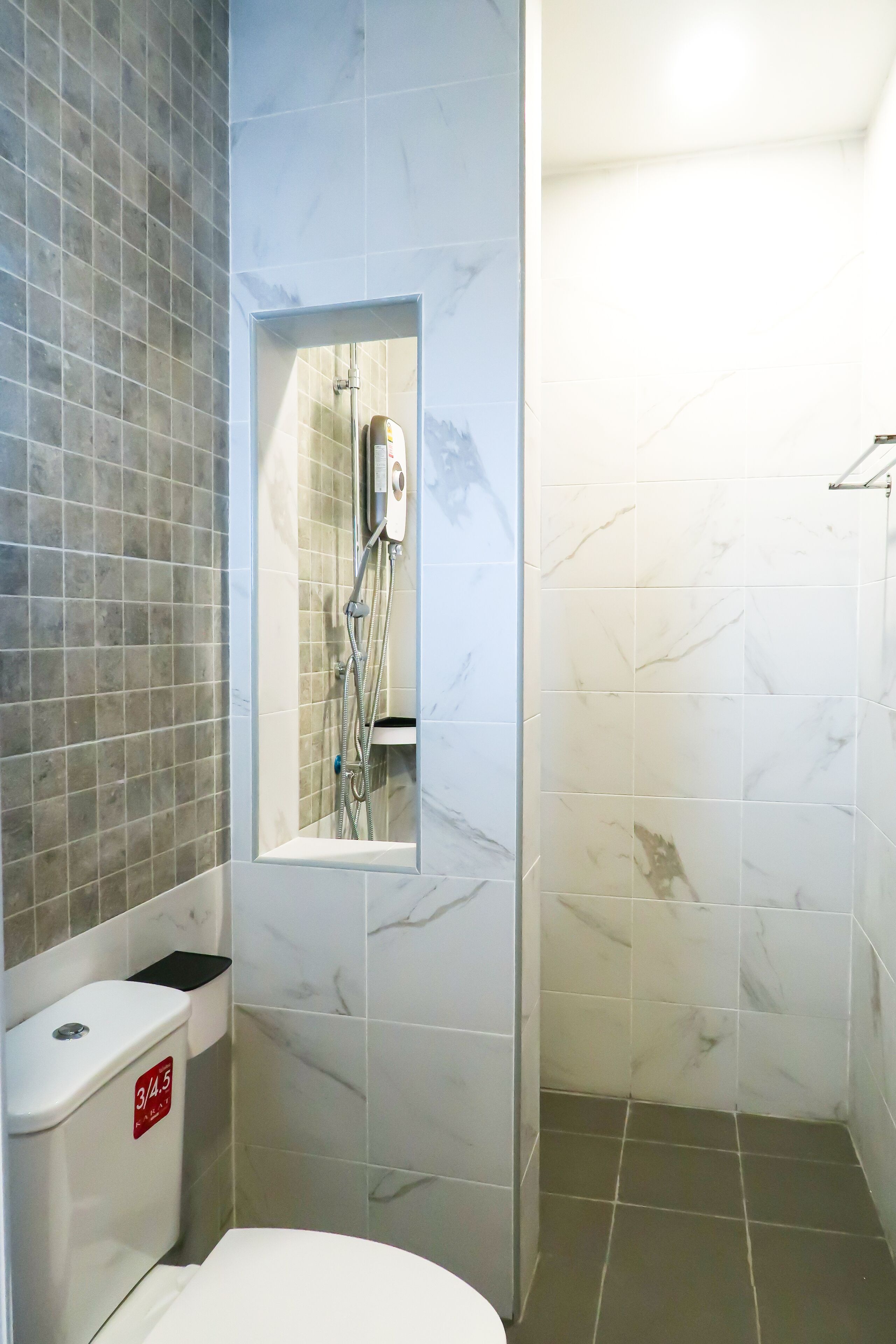 Een badkamer met toilet, douchecabine en een wand betegeld met marmer.
