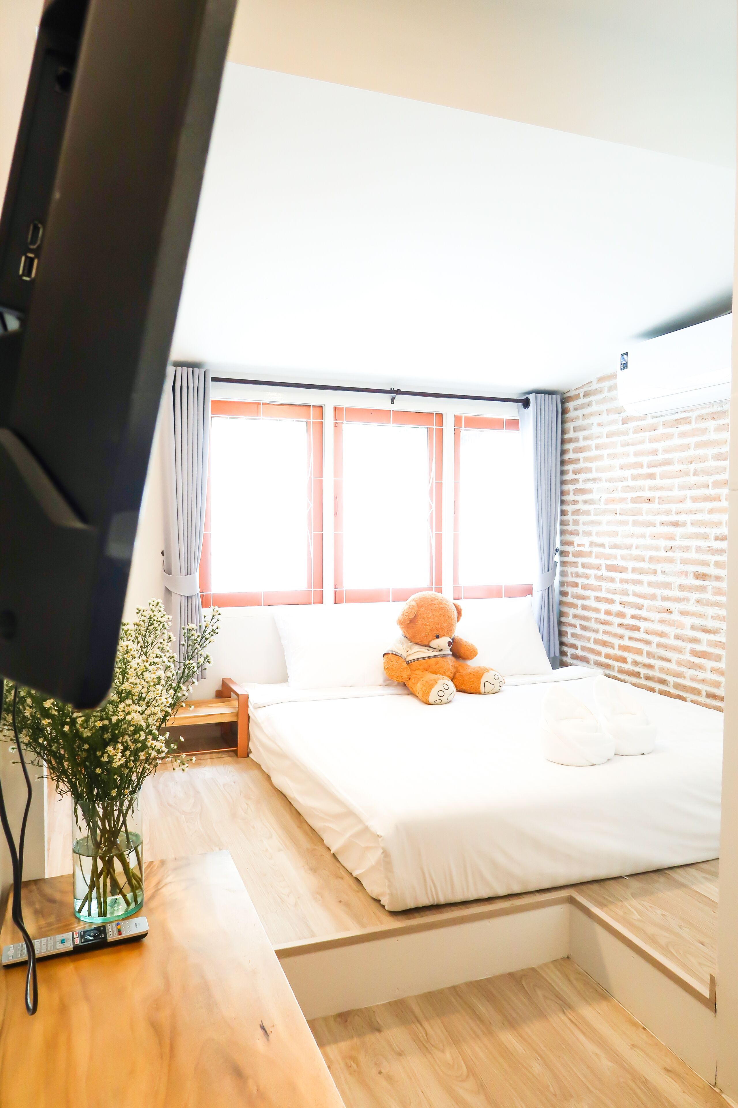 Un dormitorio con cama, un osito de peluche, televisión y ventana con cortinas.