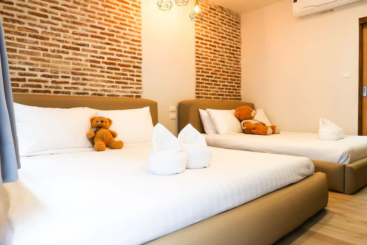 Een hotelkamer met twee bedden, elk voorzien van een teddybeer, witte kussens en een bakstenen muur.