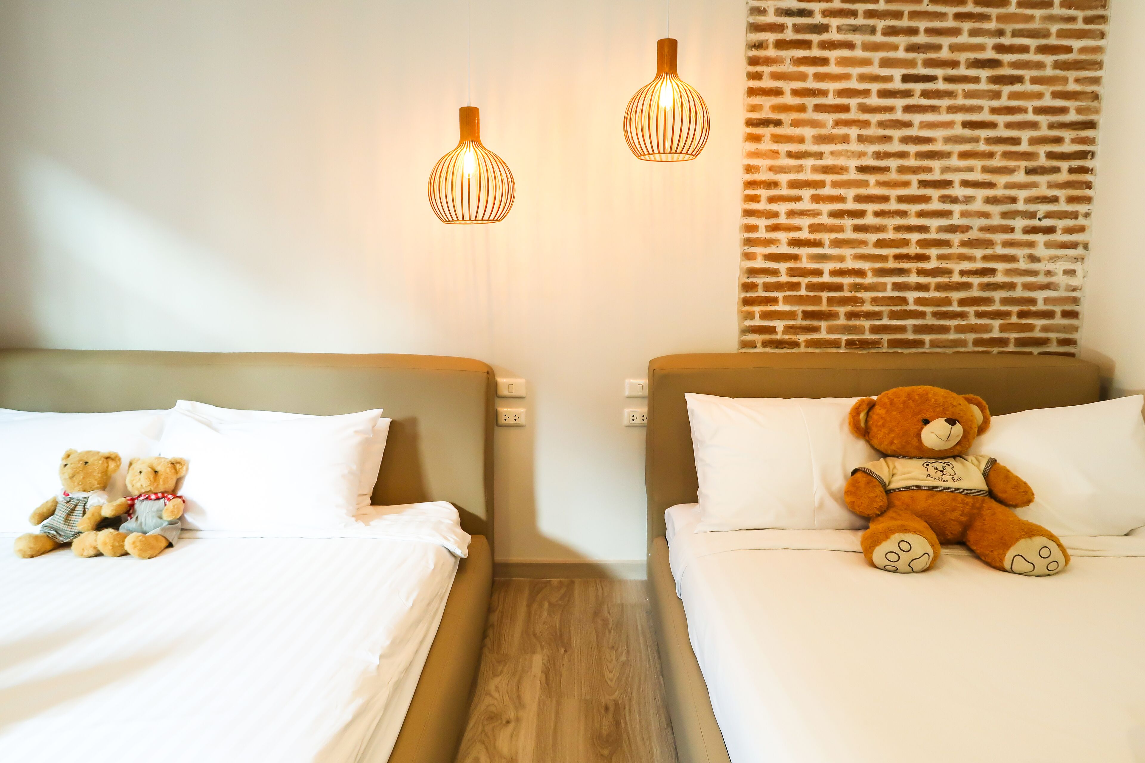 Two beds with white linens, a brick wall, and two hanging pendant lights.