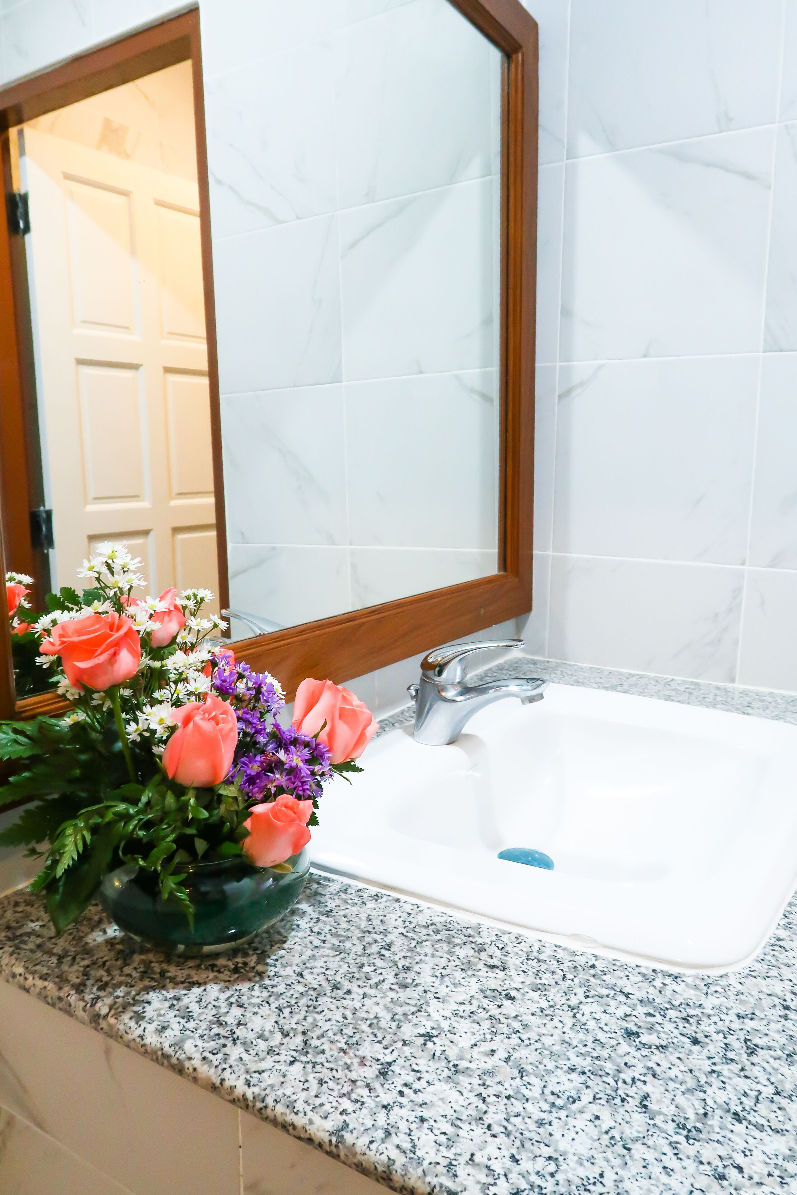 Un baño con lavamanos de mármol, espejo con marco de madera y un florero sobre la encimera.