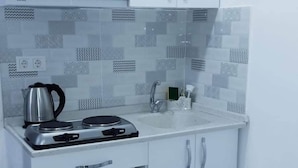 A compact kitchen with white cabinets, a gas stove, a microwave, and a sink. - Golden Life Apart Otel (Istanbul)