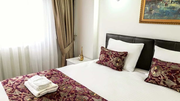 A hotel room with a neatly made bed, a nightstand with a lamp, and a painting on the wall. - Golden Life Apart Otel (Istanbul)