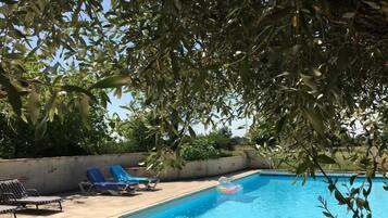 A swimming pool with blue water, surrounded by lounge chairs and trees.