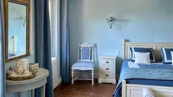 A bedroom with a bed, bedside table, chair, and a mirror.