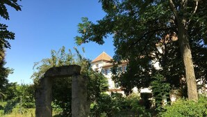 A stone archway in a garden with a building in the background. - Domaine de Menerque (Lisle-sur-Tarn)