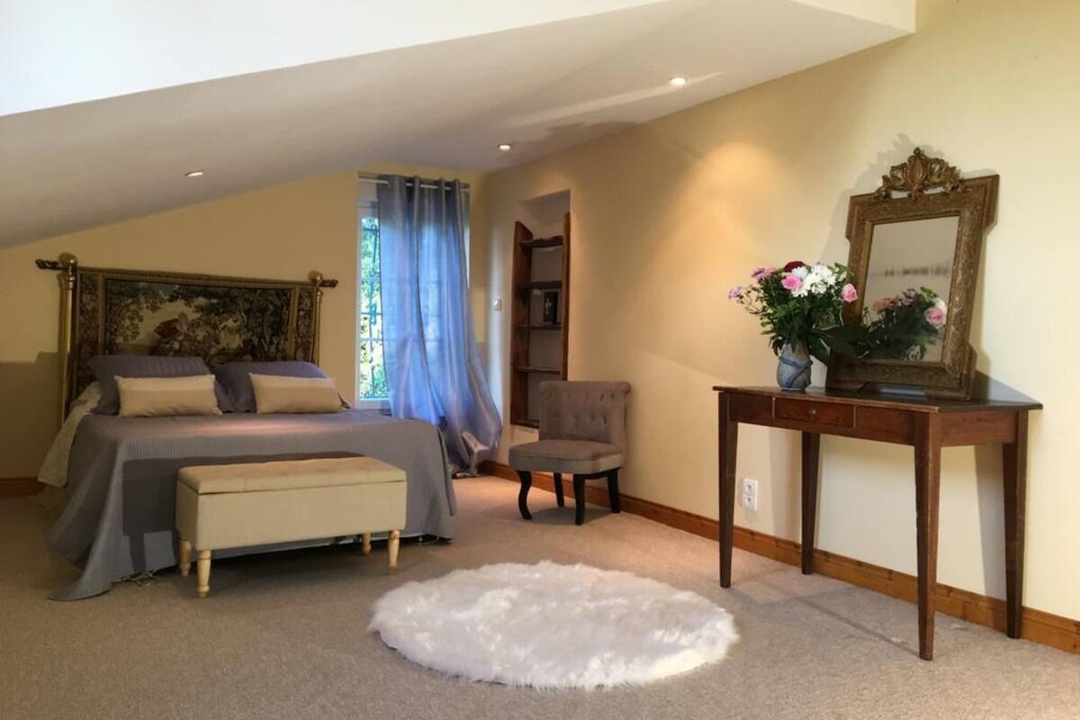 A bedroom with a bed, a chair, a small table with a mirror, and a rug.