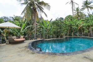 A circular pool with a surrounding stone deck, a wicker sofa with cushions, and a large umbrella. - Villa Mangga (Lembongan Island)