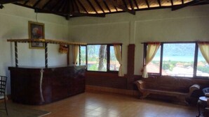 A room with a wooden reception desk, a bench, and large windows with curtains. - Villa Sinta (Baturiti)