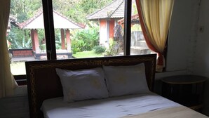 A bed with a wooden headboard, two pillows, and a white bedspread in a room with a window overlooking a garden and buildings. - Villa Sinta (Baturiti)