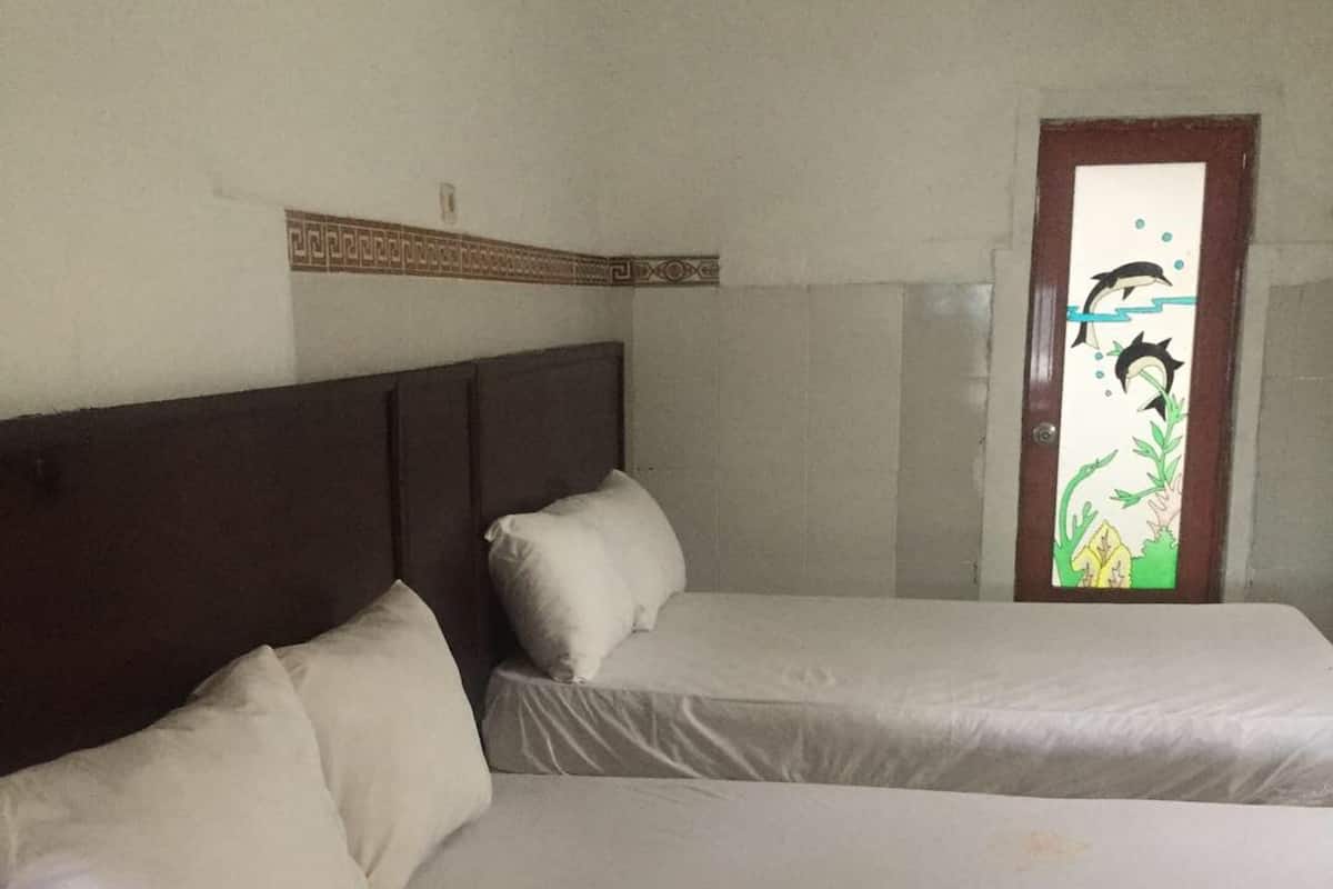 A room with two beds, each with white bedding and pillows. There is a wooden headboard on the left bed and a decorative panel above the door.