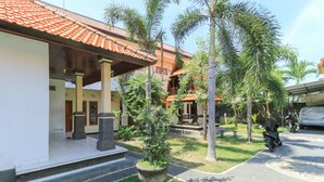 A courtyard with a tiled-roof building, palm trees, and a motorcycle parked on the pavement. - Bantan Guest House (Tibubeneng)