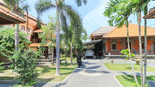A courtyard with a paved path, palm trees, and traditional architecture. - Bantan Guest House (Tibubeneng)