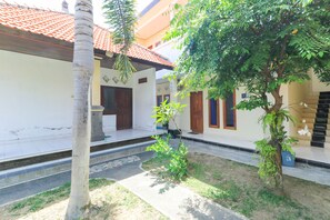 A courtyard with a palm tree, a small tree, and a building with a tiled roof and wooden doors. - Bantan Guest House (Tibubeneng)