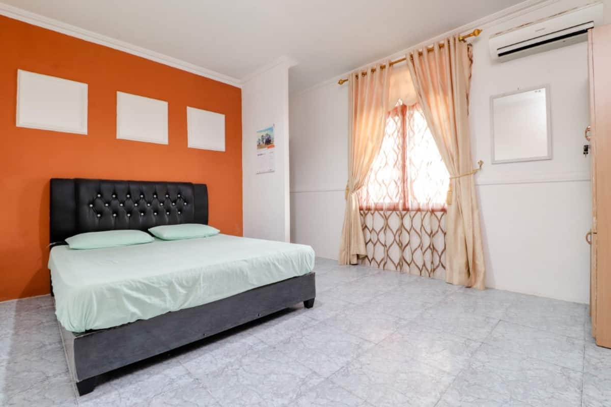 A bedroom with a bed, an air conditioner, and a window with curtains.