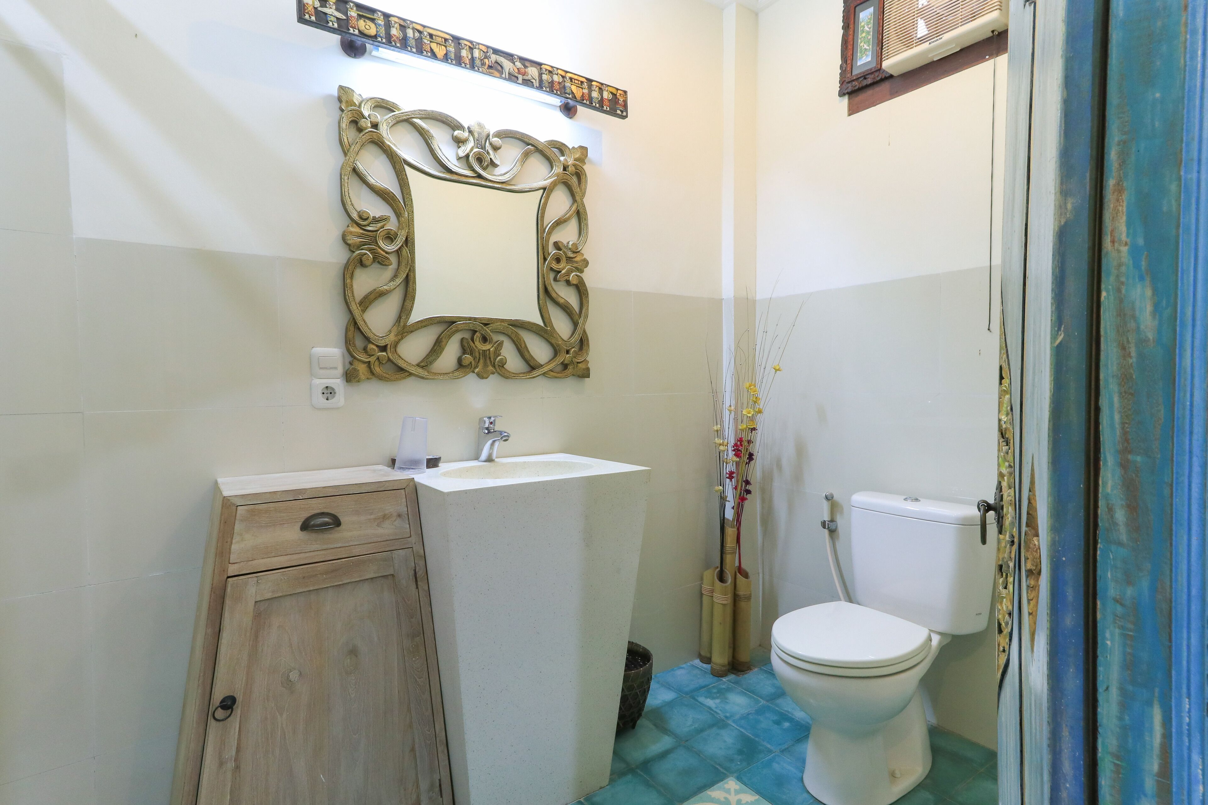 Une salle de bain avec un meuble en bois, un lavabo blanc, un miroir décoratif et des toilettes.