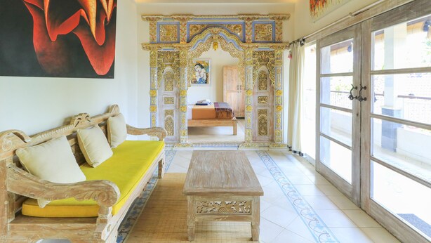 A room with a sofa, a wooden table, and a large window. - Ubud Chez Nyoman (Sukawati)