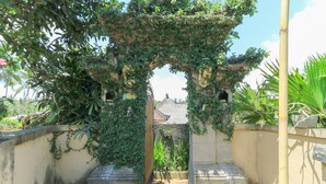 An arched entrance with a stone pathway leading to a building with a tiled roof. - Ubud Chez Nyoman (Sukawati)