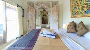 A room with a bed, a window with curtains, a painting, and a decorative archway. - Ubud Chez Nyoman (Sukawati)