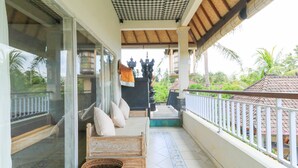 A covered balcony with a checkered ceiling, a sofa with cushions, and a woven basket. - Ubud Chez Nyoman (Sukawati)