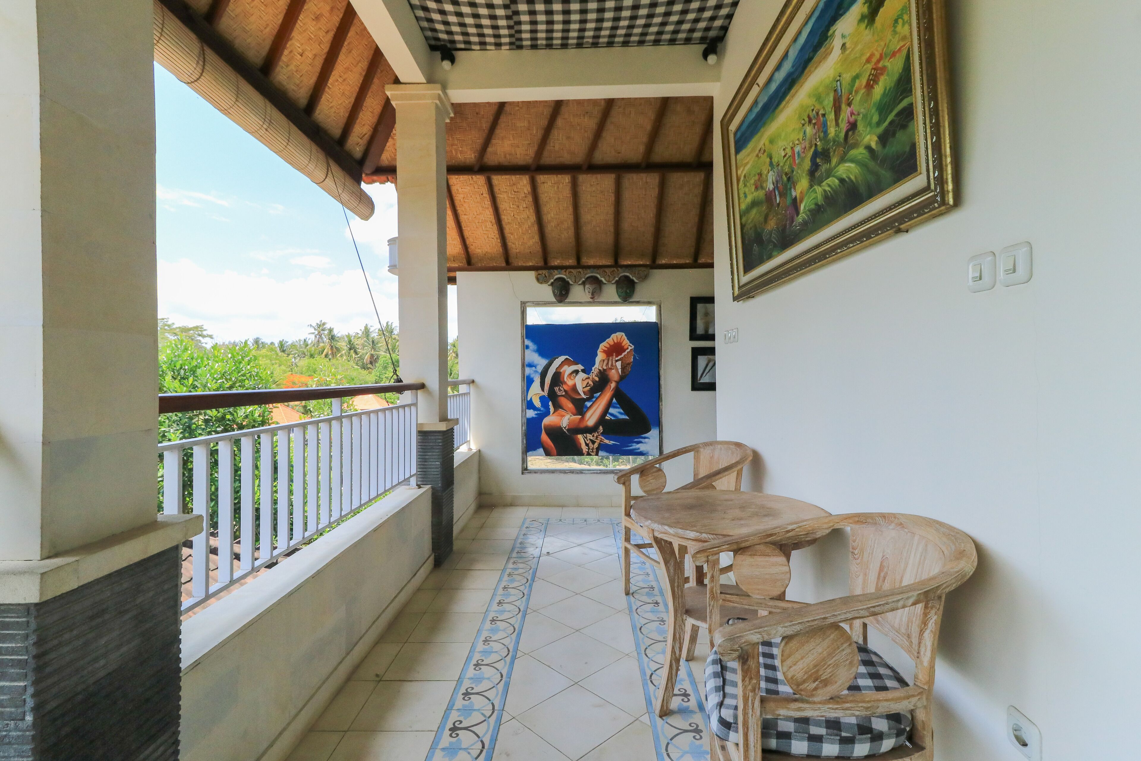 Un balcón con vista a zonas verdes, un cuadro en la pared y una mesa con sillas.