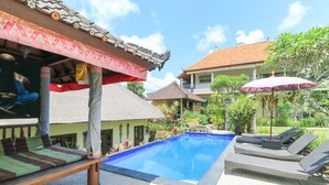 A swimming pool with lounge chairs, a thatched-roof structure, and a building with a tiled roof. - Ubud Chez Nyoman (Sukawati)